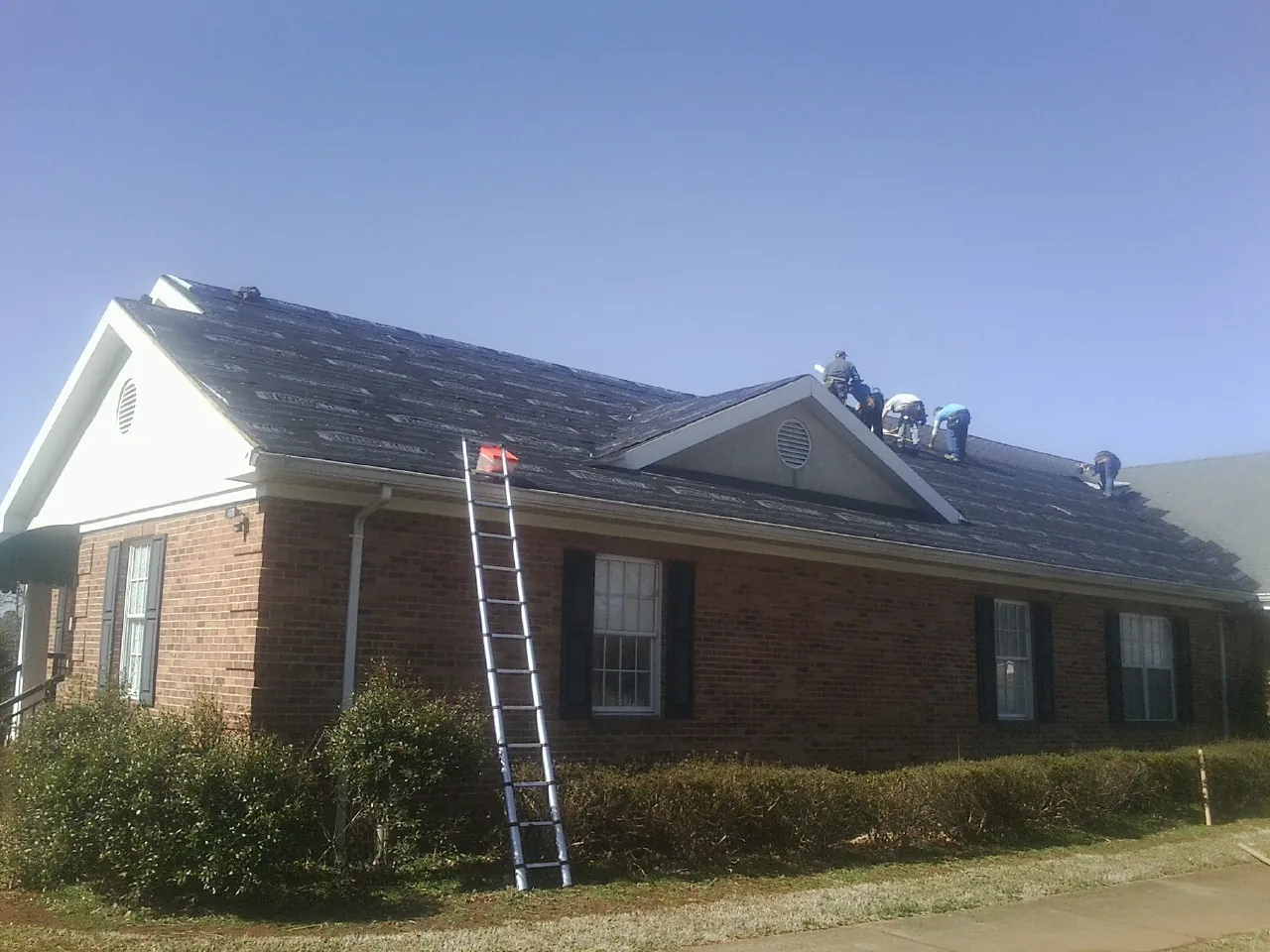 Crew tearing shingles off a brick ranch roof with a ladder set — Metal Roof Repair work by our crew in Biddeford