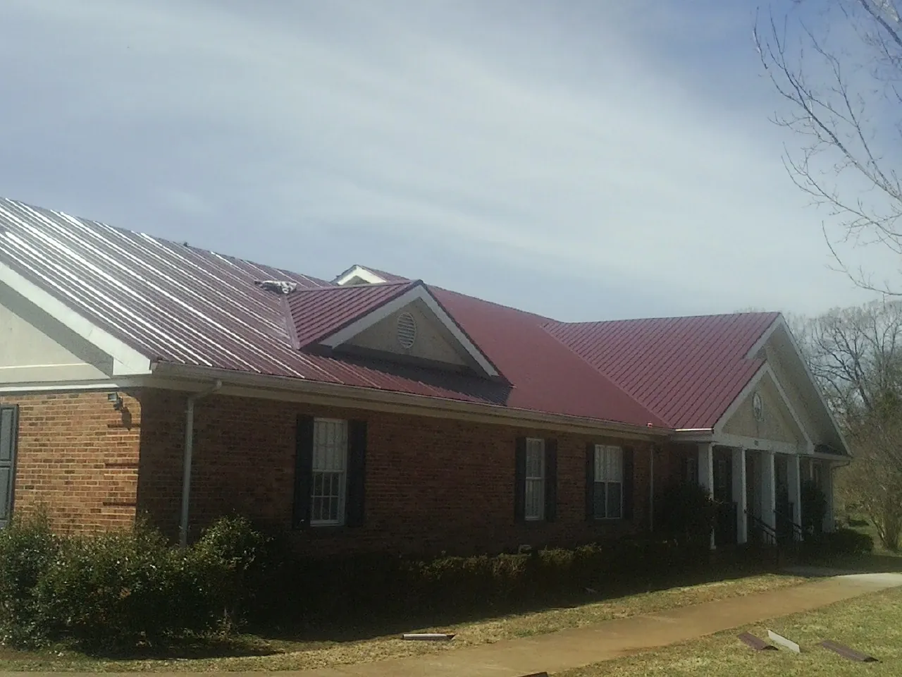 Red metal roof with gabled entries on a long brick building, from a Hail Damage Roof Repair job in Biddeford