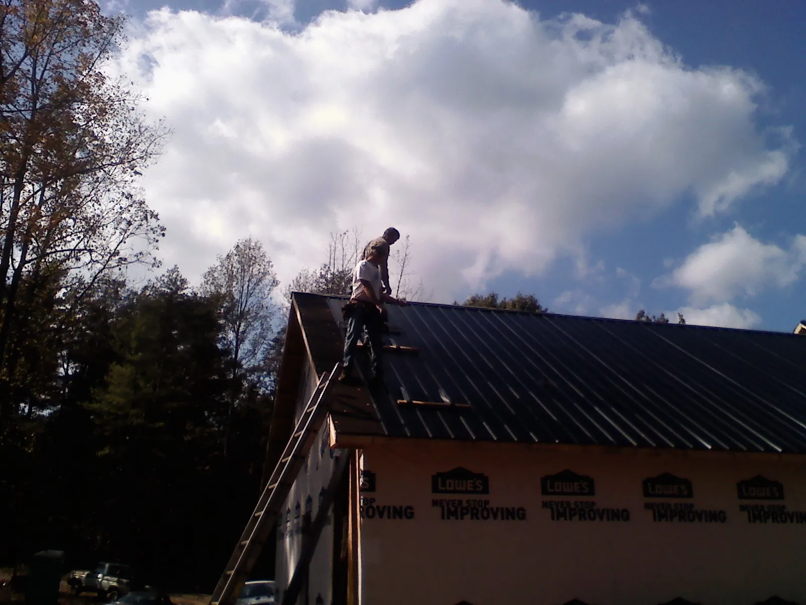 Roofer fastening dark metal panels high against a cloudy sky, from a Roof Inspection job in Biddeford