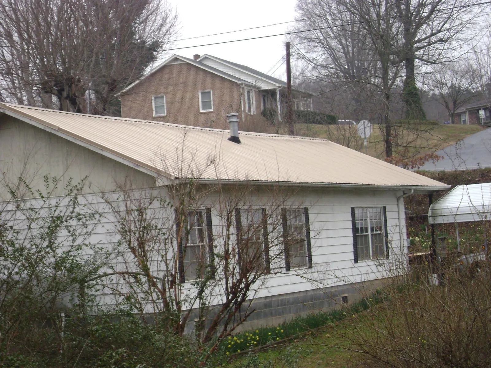 Tan metal roof on a white sided house set into a hillside — Commercial Roofing by Roofing Brothers in Biddeford