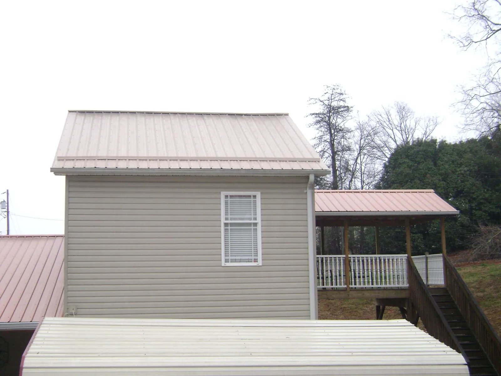 Tan metal roofs on a two story addition and attached porch, from a Roof Replacement job in Biddeford